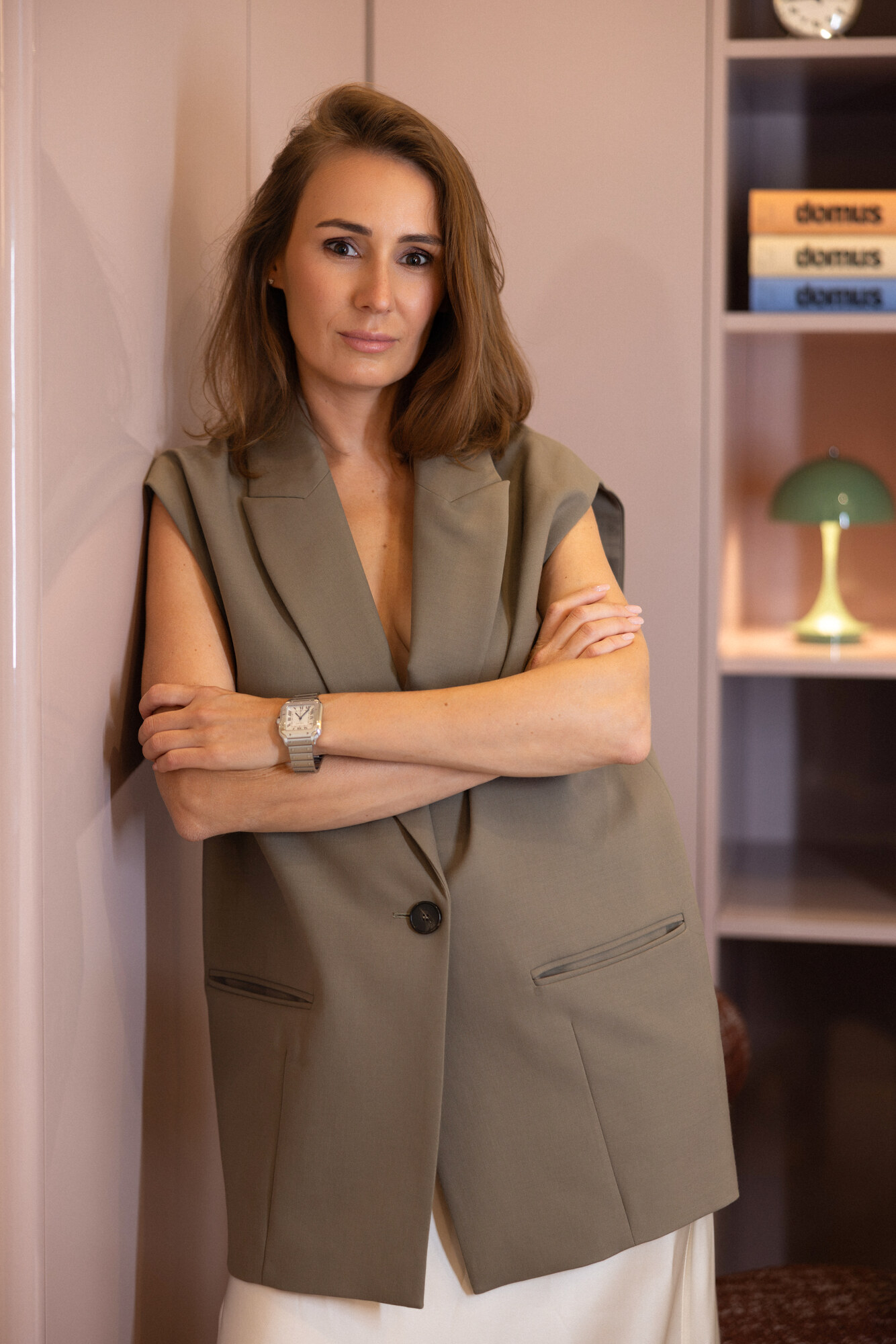Aline Eremeeff — portrét designérky se zkříženýma rukama u zdi s knihovnou